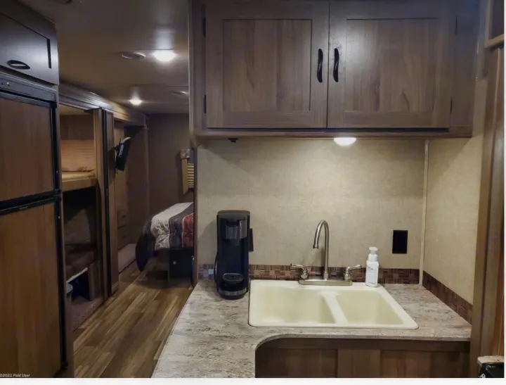 Inside an RV rental: full kitchen with double sink & coffee maker, leading to bunk beds & a private bedroom. Ideal for travel.. Coachmen Freelander 31BH 2017