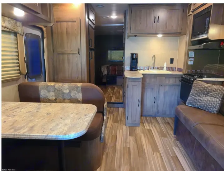 Inside this cozy RV rental: A bright dinette, kitchen with microwave & stove, plus a glimpse of the back bedroom.. Coachmen Freelander 31BH 2017