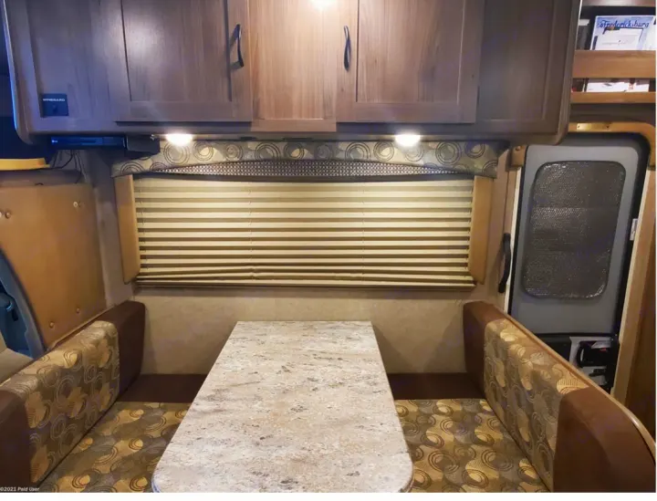 Experience comfort in this RV rental's dinette area, featuring a table, patterned benches, and overhead cabinets.. Coachmen Freelander 31BH 2017