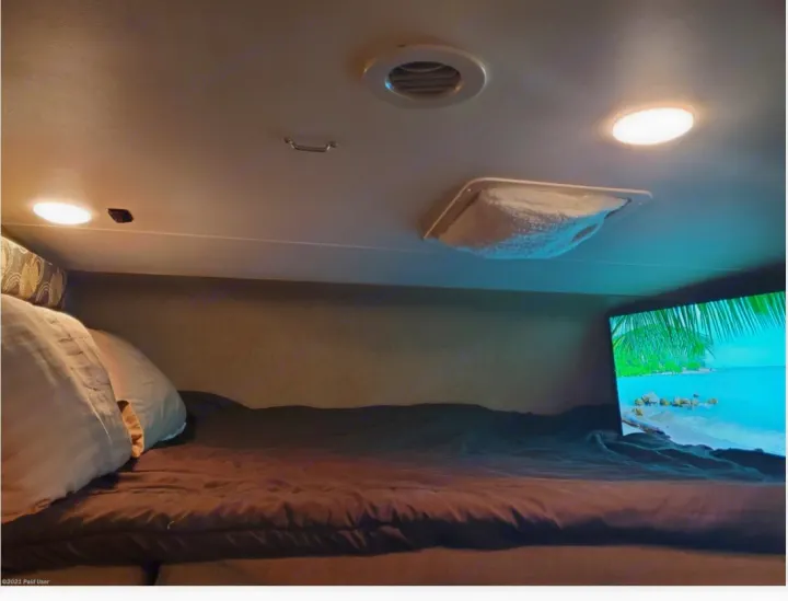 Cozy rv rental sleeping area with frosted AC vent, a comfortable bed, and a TV for entertainment.. Coachmen Freelander 31BH 2017