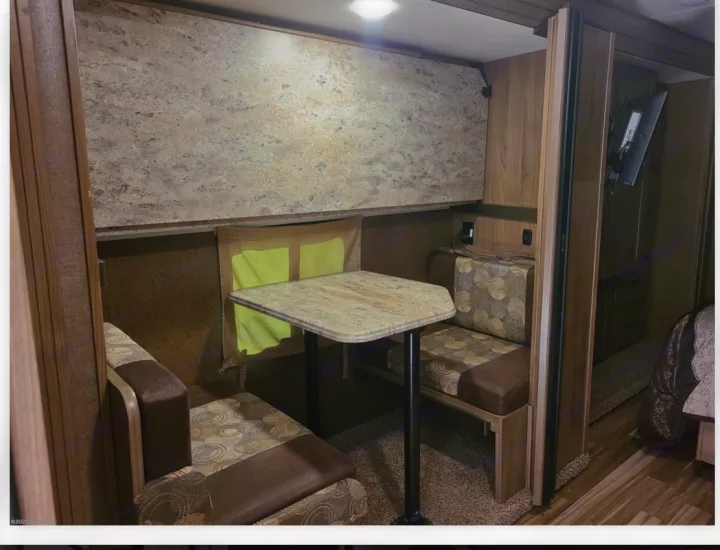 RV rental interior: a cozy dinette with a light-colored table and patterned upholstered benches, surrounded by wood trim.. Coachmen Freelander 31BH 2017