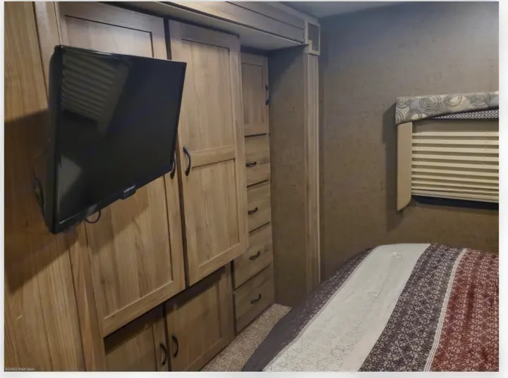 RV rental bedroom with wall-mounted TV, integrated wooden storage cabinets, and a comfortable bed.. Coachmen Freelander 31BH 2017