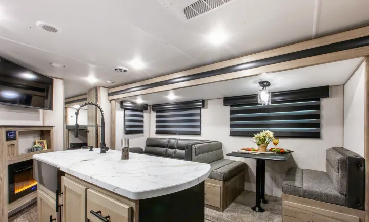 Bright RV rental interior with a white-marbled kitchen island, gray dining booth, and sofa seating.. Forest River Cherokee Wolf Pack 2021