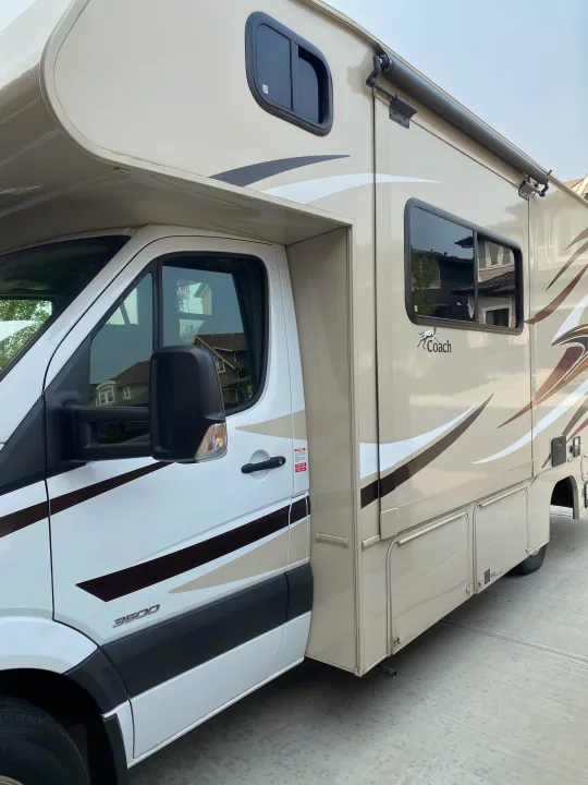 A tan and white Class C RV rental, likely a Mercedes-Benz Sprinter-based motorhome, parked on concrete.. Coachmen Prism 2016