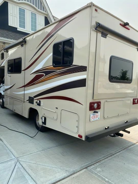 Tan RV rental showing side & rear view, power cord plugged in. Perfect for your next travel adventure!. Coachmen Prism 2016