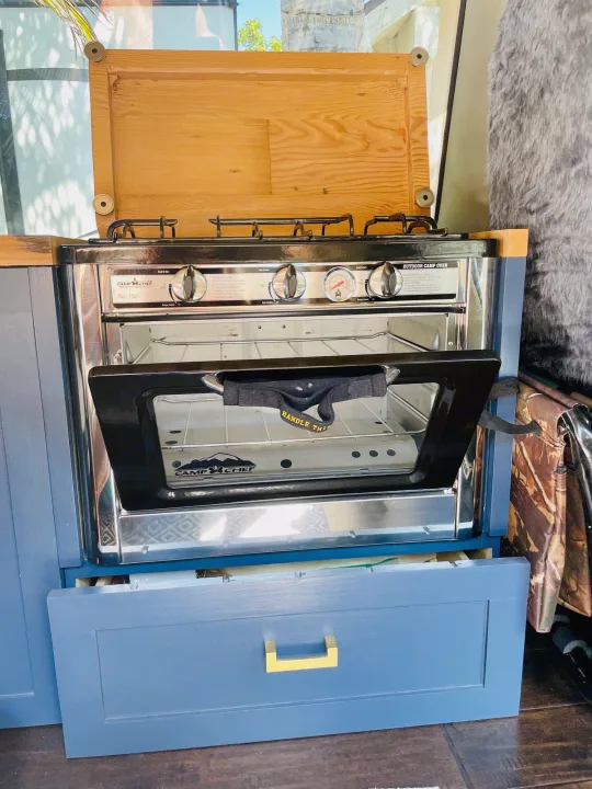 RV rental kitchen showcasing a Camp Chef outdoor camp oven and stove, built into custom blue cabinetry with an open drawer.. Chevrolet Astro Van AWD 2003