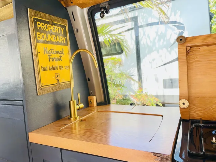 Cozy RV rental kitchen with golden faucet, wooden sink/countertop, and stove. Perfect for mobile adventures!. Chevrolet Astro Van AWD 2003