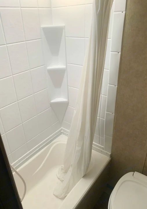 Clean and compact white shower-tub unit within an RV rental bathroom, complete with built-in shelves and shower curtain.. Coachmen Clipper 2015