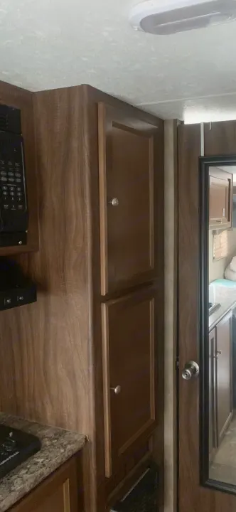 RV rental interior: Compact kitchen with microwave, wooden cabinets, and speckled countertop, showing functional living space.. Coachmen Clipper 2015