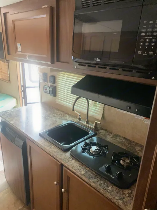 This RV rental kitchen features a microwave, sink, stove, and compact refrigerator, offering all amenities for cooking on the go.. Coachmen Clipper 2015
