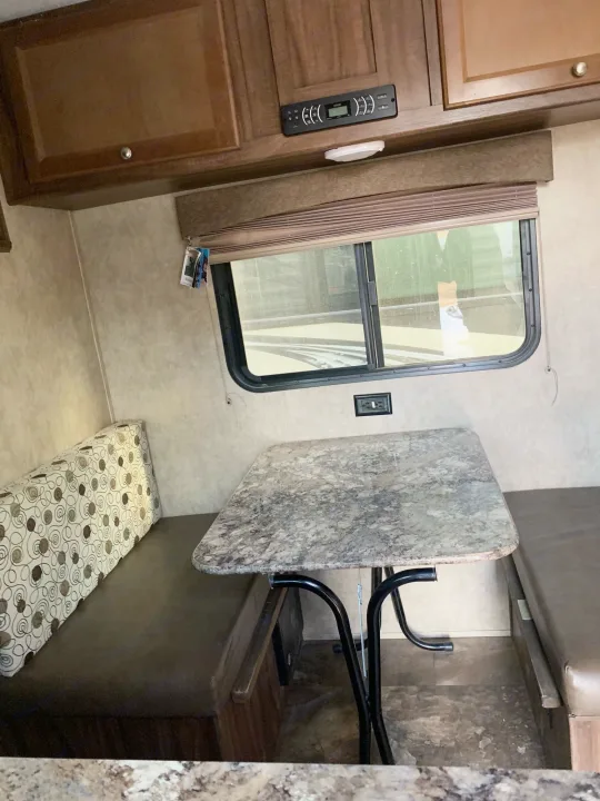 RV rental dinette: Features booth seating, a speckled table, wood cabinets, and a window, ideal for meals or relaxing.. Coachmen Clipper 2015