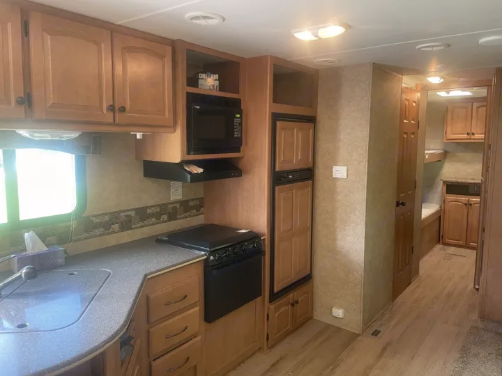 RV rental interior: A functional kitchen with sink, stove, microwave, fridge, and ample cabinets. Features light wood trim & bunks.. Heartland North Country Lakeside 2011