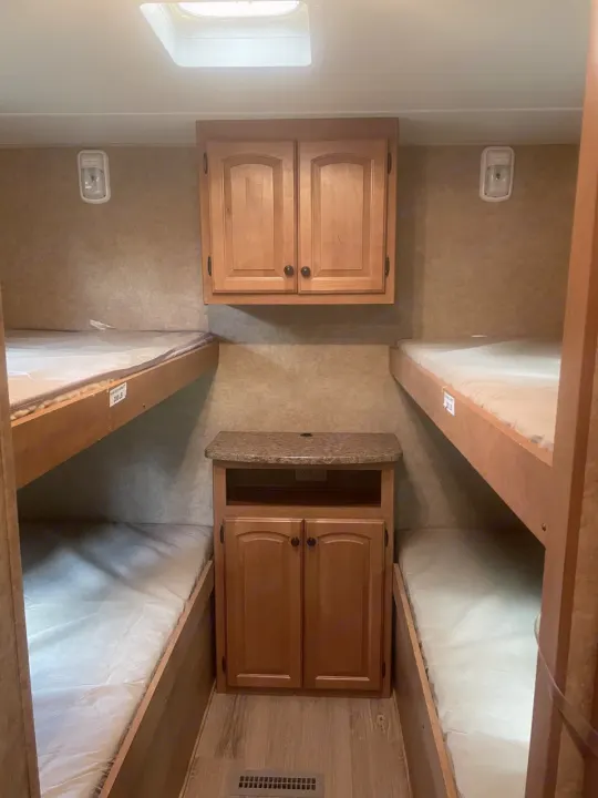 RV rental bunk room: four beds (bunks) on both sides, with a central storage cabinet. Bright interior with a skylight.. Heartland North Country Lakeside 2011