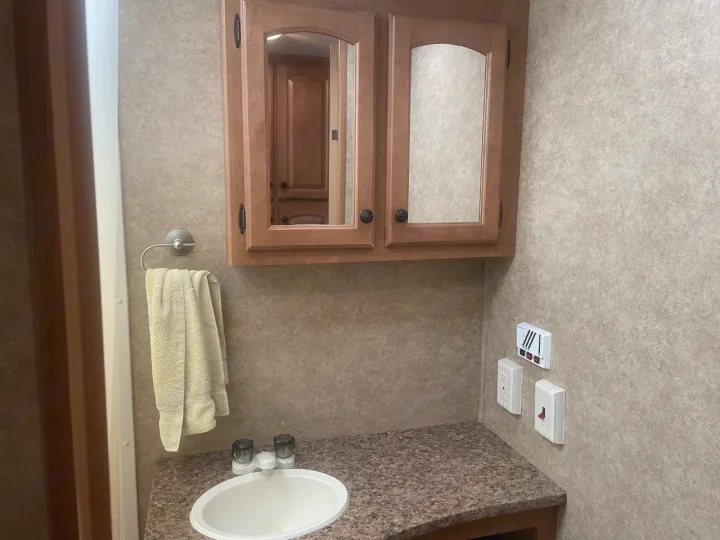 RV rental bathroom with wooden medicine cabinet, sink, towel rack, and wall controls including an outlet.. Heartland North Country Lakeside 2011