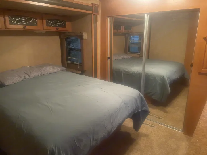 Cozy RV rental bedroom features a comfortable bed with light blue duvet, striped pillows, overhead cabinets, and mirrored closet.. Heartland North Country Lakeside 2011