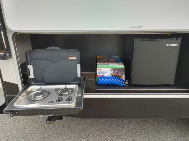 RV rental outdoor kitchen setup: pull-out stove, RVISION mini-fridge, and camping gear including a PIC insect killer torch.. Starcraft Travel Trailer 2021