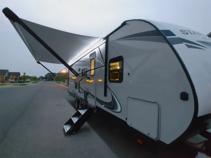 Explore with an RV rental! This white travel trailer is illuminated at dusk, featuring a deployed awning and steps.. Starcraft Travel Trailer 2021