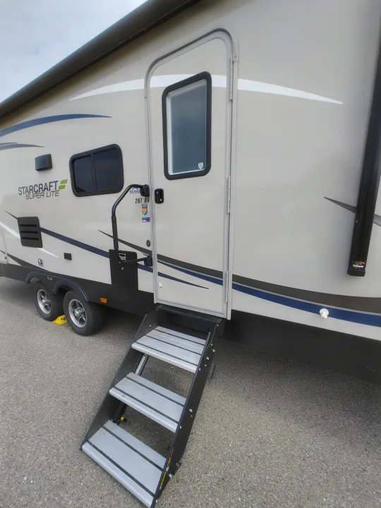 This Starcraft Super Lite RV rental features a tan exterior with blue stripes, accessible via extended steps and an entry door.. Starcraft Travel Trailer 2021