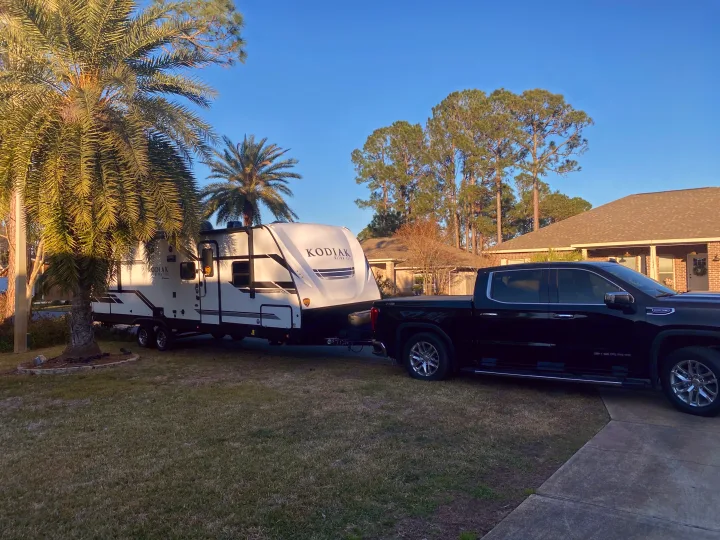 Sunny day RV rental setup: A black pickup truck is hitched to a white Kodiak travel trailer in a suburban yard with palm trees.. Dutchmen Kodiak 2021
