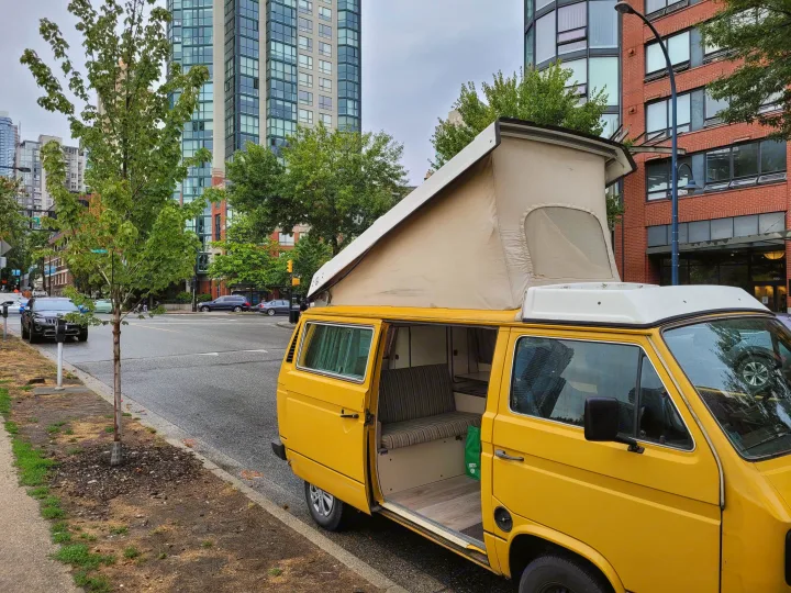 A bright yellow pop-top camper van, possibly an RV rental, is parked on a city street, revealing its interior.. Volkswagen Westfalia 1982