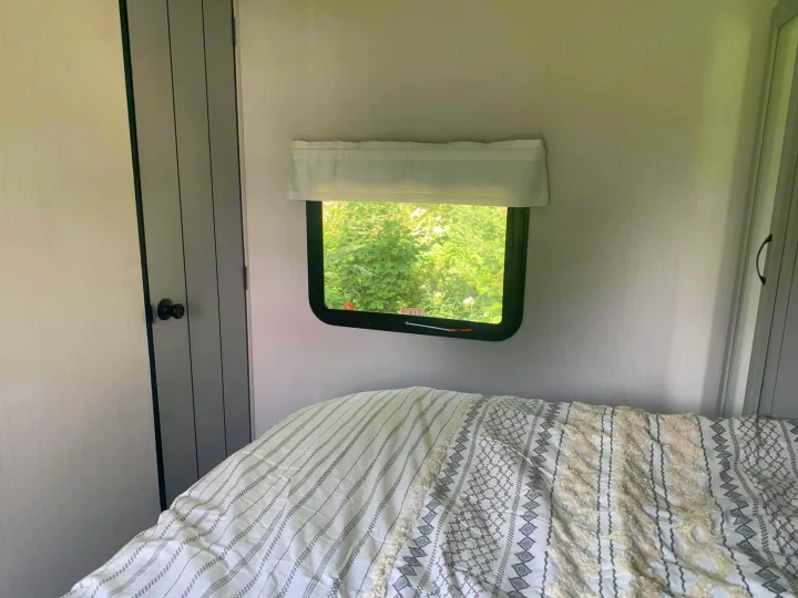 Cozy RV rental bedroom featuring a comfy patterned bed, window with green nature view, and built-in closets.. Forest River Vibe 2021