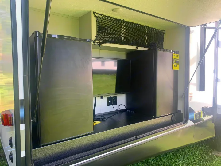 RV rental's outdoor entertainment center: features two mini-fridges, a TV, and overhead storage net in a side compartment.. Forest River Vibe 2021