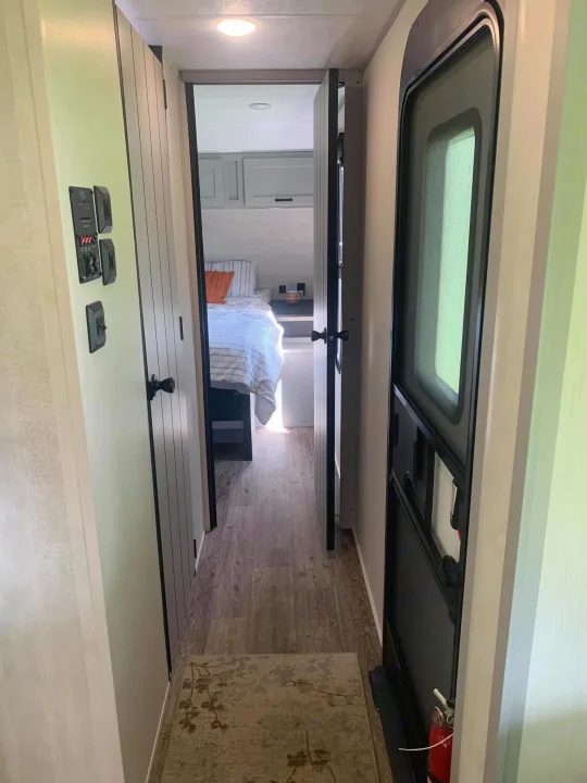 Inside this RV rental: A hallway shows a control panel, a bedroom entrance, and the main entry door with a fire extinguisher.. Forest River Vibe 2021
