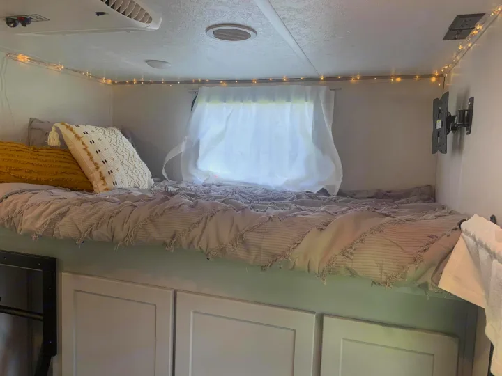 Cozy RV rental interior: a comfortable bunk bed with pillows, illuminated by fairy lights, above storage cabinets.. Forest River Vibe 2021