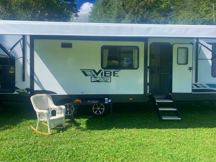 Enjoy outdoor living with this VIBE RV rental. Features an awning, steps, and a cozy wicker chair on lush grass.. Forest River Vibe 2021