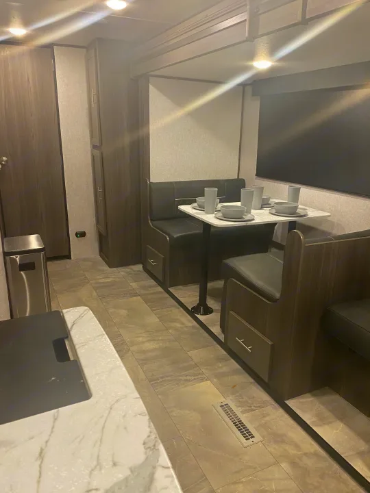 RV rental interior featuring a modern dinette with booth seating, a set table, and a partial kitchen area with tiled flooring.. Dutchmen Kodiak 2021