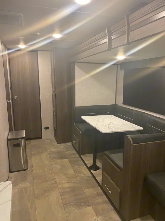 RV rental interior: A compact dinette with dark benches and a white table, alongside sleek storage and tiled flooring.. Dutchmen Kodiak 2021