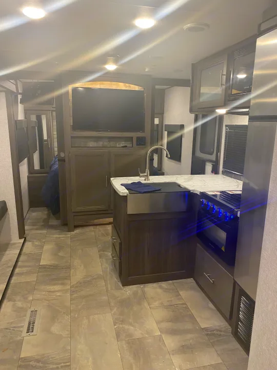 Modern RV rental interior. Features a well-equipped kitchen with a large sink, stove, and microwave, plus a TV area.. Dutchmen Kodiak 2021