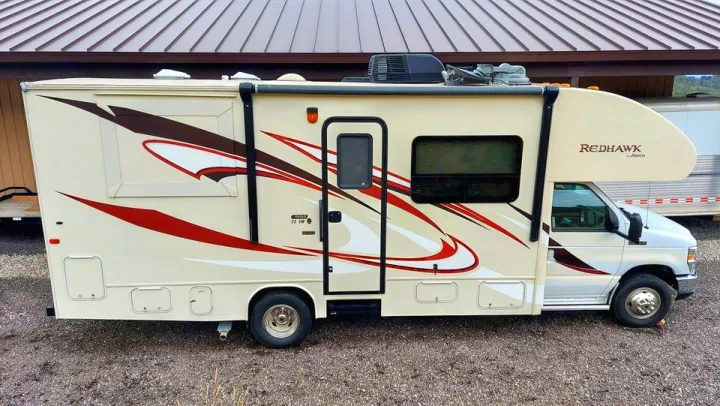 Cream Jayco Redhawk RV rental, a Class C motorhome with red/brown graphics and awning, ideal for road trips.. Jayco Redhawk 2016