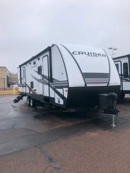 A white and black Cruiser Aire travel trailer, a potential RV rental, parked on a wet asphalt lot. Ready for outdoor adventures.. Crossroads Cruiser Aire 2021