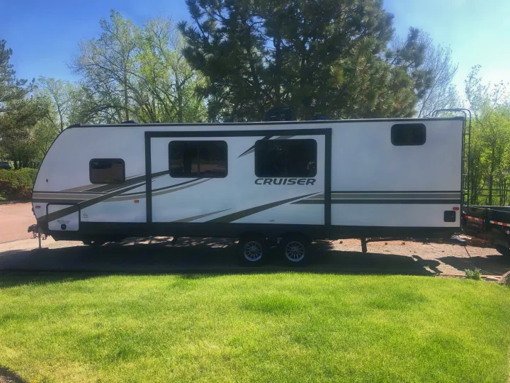 Side view of a white Cruiser travel trailer parked on pavement near grass and trees, perfect for an RV rental.. Crossroads Cruiser Aire 2021