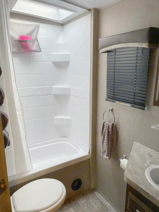 Compact RV rental bathroom features a shower-tub combo, toilet, vanity with sink, and a window with blinds.. Forest River Rockwood Mini Lite 2020