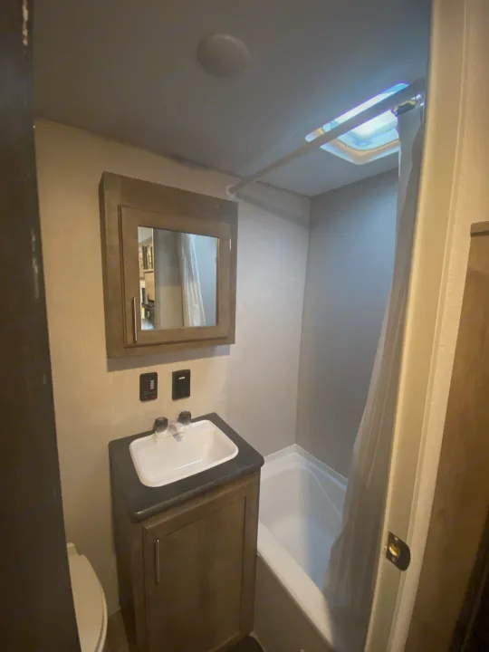 RV rental bathroom featuring a toilet, sink vanity with mirrored medicine cabinet, and a bathtub/shower with a skylight.. K-Z Manufacturing Sportsman Classic 2021