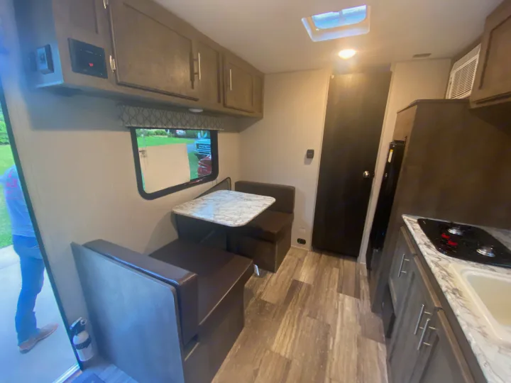 RV rental interior showing a dinette with table & benches, compact kitchen (stove & sink), and storage cabinets.. K-Z Manufacturing Sportsman Classic 2021