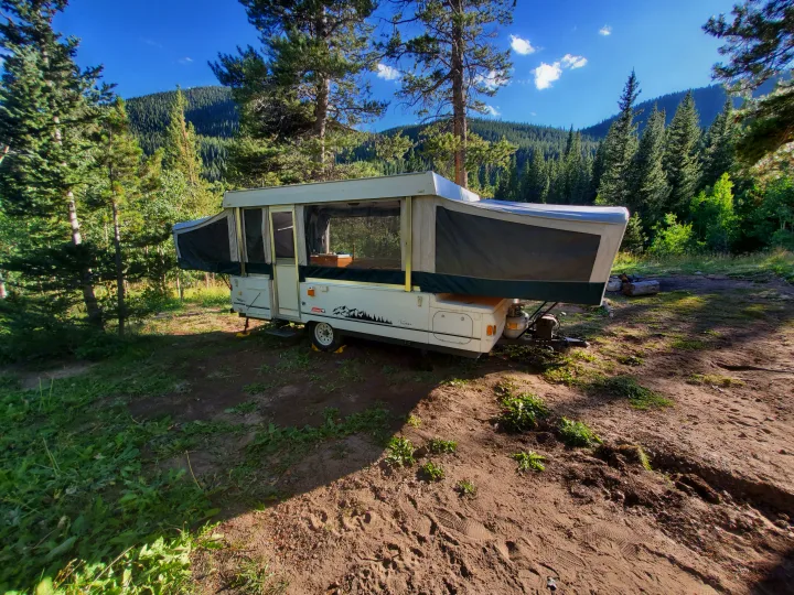 Pop-up camper RV rental set up in a scenic mountain forest campsite. Ideal for outdoor adventures.. Coleman Fairlake 2002