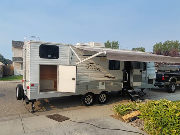 Travel trailer RV rental setup: awning extended, doors open, parked and set up in a residential driveway. Ready for your trip!. Keystone Springdale 2010
