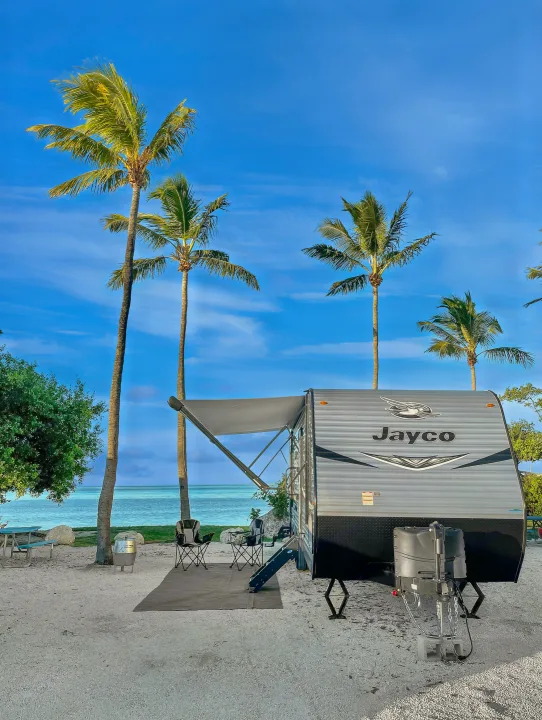 Beachfront bliss! This Jayco RV rental is set up under palm trees by turquoise waters, offering a perfect tropical escape.. Jayco Jay Flight 2021