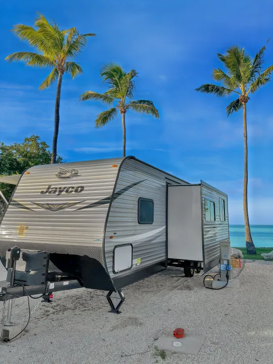 Jayco RV rental at a tropical beachfront campsite with palm trees and turquoise water under a clear blue sky.. Jayco Jay Flight 2021