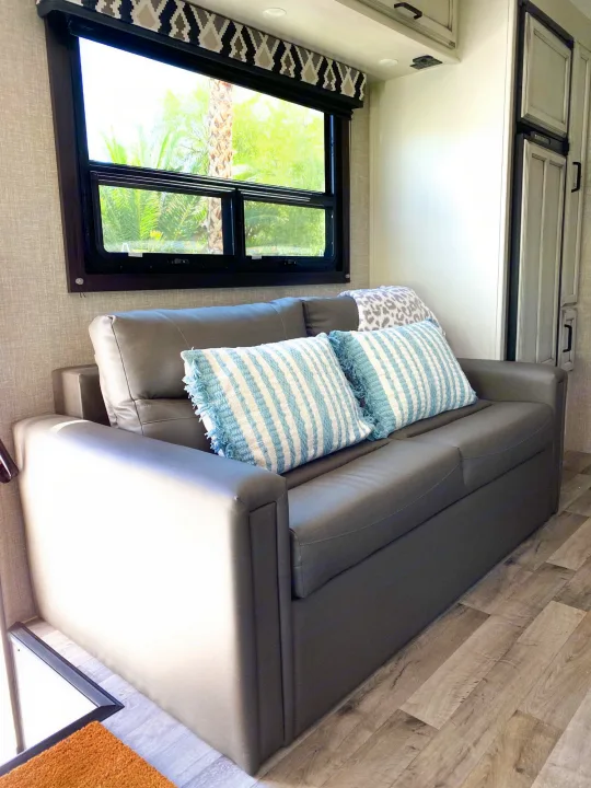 Inside an RV rental: a comfortable gray sofa with blue striped pillows, a window with outdoor views.. Entegra Coach Other 2022