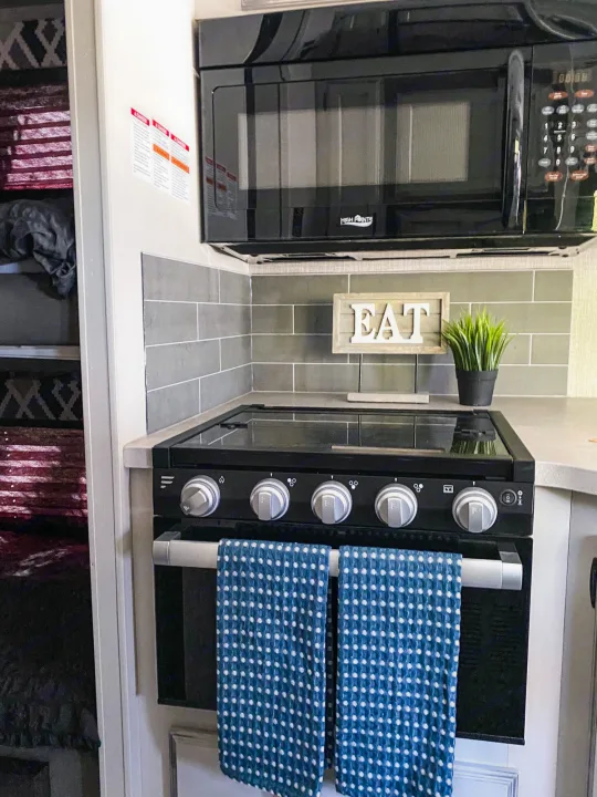 Inside an RV rental: a compact kitchen with a black microwave, stove, tiled backsplash, and homey decor.. Entegra Coach Other 2022