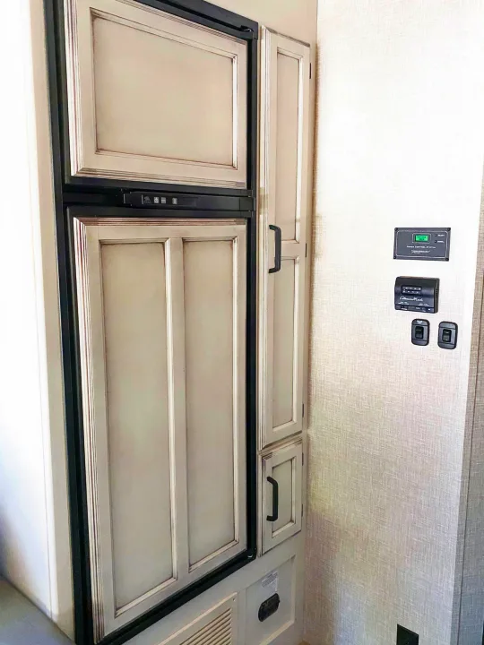 Inside an RV rental: kitchen fridge with cabinet doors, pantry, and essential control panels for comfortable camping.. Entegra Coach Other 2022