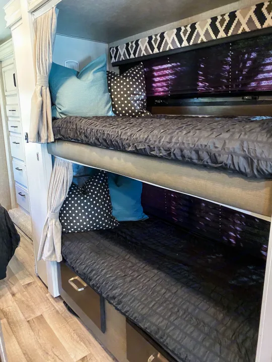 Cozy RV rental bunk beds with dark bedding, blue & polka dot pillows, and privacy curtains for comfortable travel.. Entegra Coach Other 2022