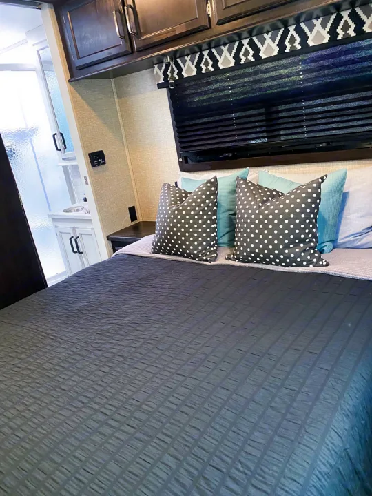 Cozy RV rental bedroom featuring dark gray bedding, polka dot pillows, and a glimpse of the attached bathroom with a sink.. Entegra Coach Other 2022