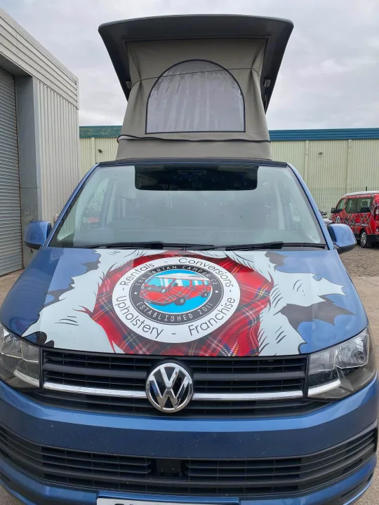 Blue VW pop-top campervan with Scottish tartan branding for rv rental, conversions, and upholstery. A red van is visible behind.. Volkswagen T5 2018