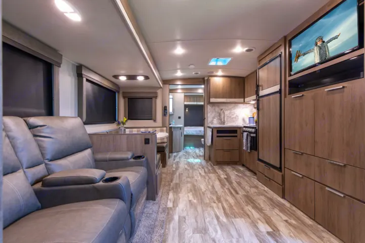 Modern RV rental interior: lounge with recliners, full kitchen, dinette, and bedroom beyond. Ideal for comfortable travel.. Grand Design Imagine 2022