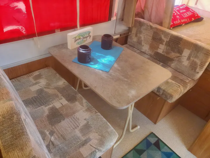 Inside an RV rental: a cozy dinette with patterned benches, a table, and red pop-up camper windows.. Viking 1906st 2004
